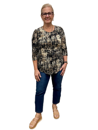 Woman standing in a fitting room wearing a patterned top and blue jeans.