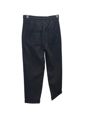 Black pants hanging on a clear hanger against a white wall.