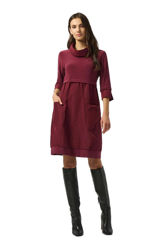 Woman wearing a burgundy dress with long sleeves and black knee-high boots on a white background