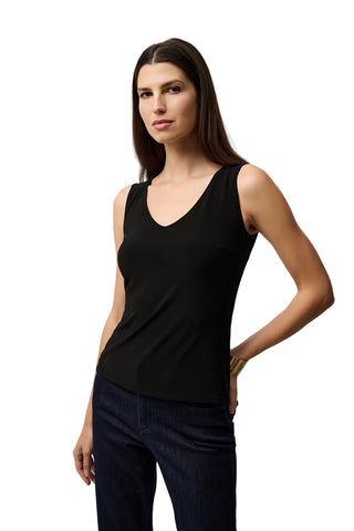 Woman wearing a black tank top and dark jeans against a light gray background