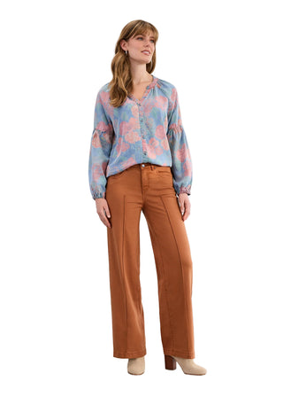 Woman wearing a floral blouse and brown pants against a white background