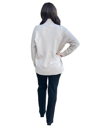 Person wearing a beige sweater and dark pants standing in front of a store entrance with decorative plants.