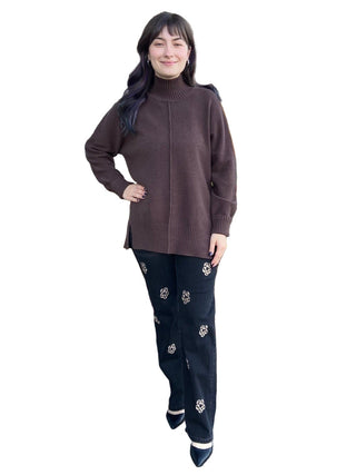 Woman in a brown sweater and black pants standing in front of a store with fall decorations.
