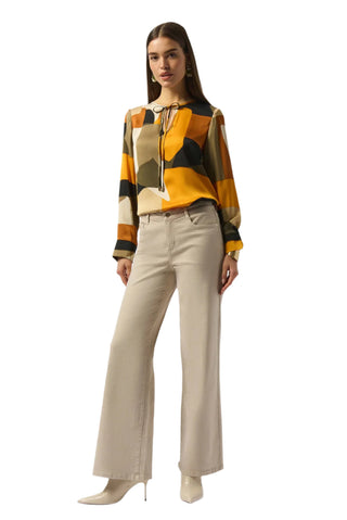 Woman wearing a patterned blouse and beige pants on a white background