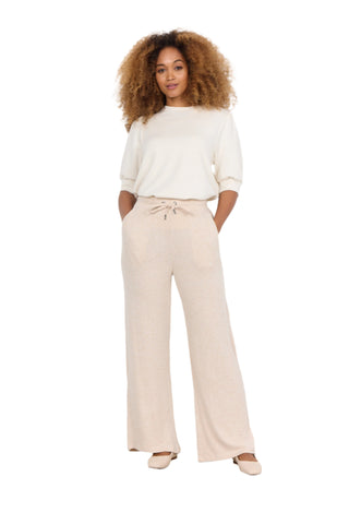 Woman wearing a white top and beige wide-leg pants on a plain background