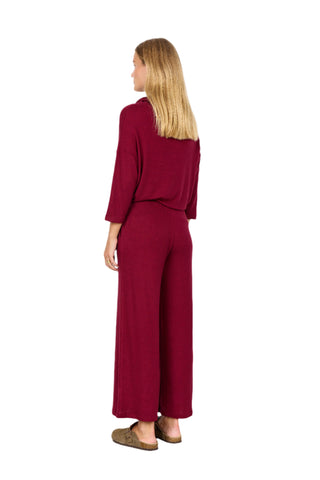 Woman wearing a burgundy outfit with wide-leg pants against a white background
