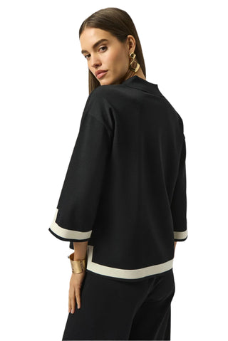 Woman wearing a black outfit with white trim on a plain background