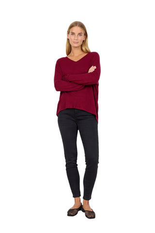 Woman wearing a burgundy sweater and black pants against a white background