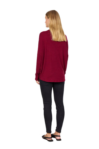 Woman wearing a burgundy sweater and black pants against a white background