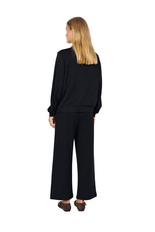 Woman wearing a black outfit with wide-leg pants against a white background