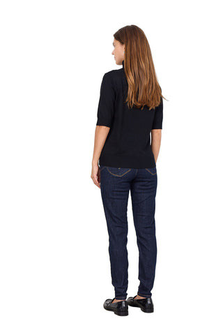 Woman wearing a black top and dark blue jeans against a white background