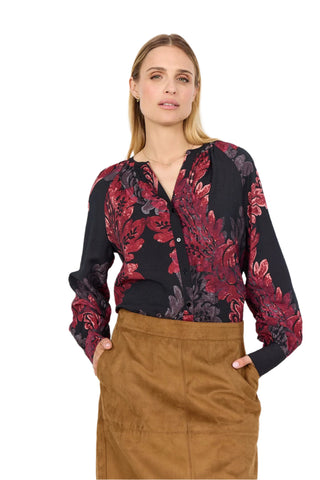 Woman wearing a black floral blouse with red and purple patterns against a white background