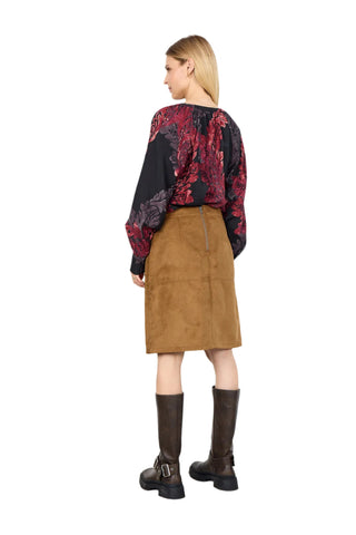 Woman wearing a patterned top, brown skirt, and black boots on a white background