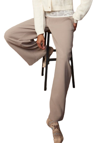 Woman in a white cardigan and beige pants sitting on a chair against a brown textured background