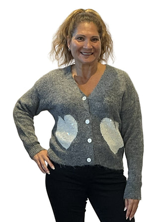 Woman wearing a gray cardigan with heart patterns on a plain background