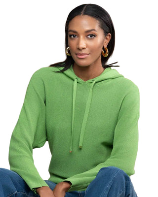 Woman wearing a green hoodie sitting on a couch with a wooden wall background