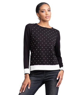 Woman wearing a black sweater with white polka dots and dark jeans on a gray background
