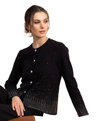 Woman wearing a black beaded cardigan sitting on a brown leather couch with a wooden paneled wall in the background.