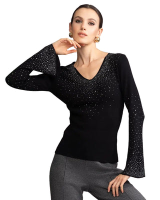Woman wearing a black long-sleeve top with embellishments against a gray background