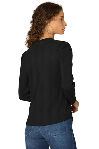 Woman wearing a black long-sleeve top and blue jeans on a plain background