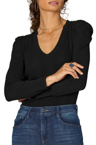 Woman wearing a black top and blue jeans against a neutral background