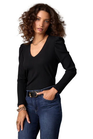 Woman wearing a black long-sleeve top and blue jeans against a gray background