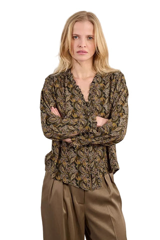 Woman wearing a patterned blouse and beige pants against a plain background