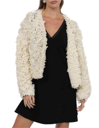 Woman wearing a textured white cardigan over a black dress on a white background