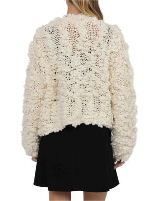 Person wearing a textured white sweater over a black skirt on a white background