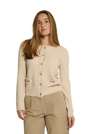 Woman wearing a beige ribbed sweater and beige pants against a white background