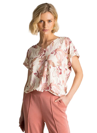 Woman wearing a floral blouse and pink pants against a neutral background