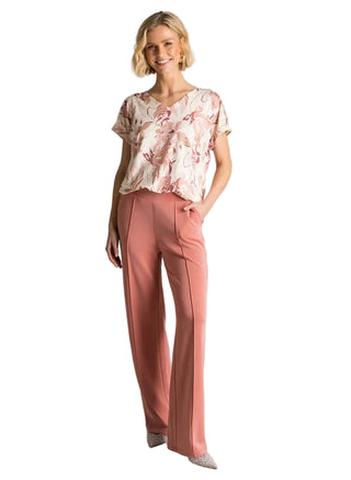 Woman wearing a floral top and pink pants against a plain background