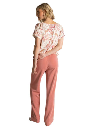 Woman wearing a floral top and pink pants against a plain background