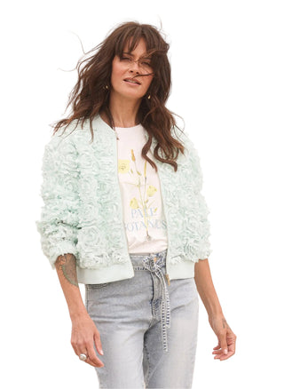 Woman wearing a light green bomber jacket over a graphic t-shirt with a desert background
