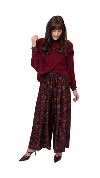 Woman wearing a burgundy sweater and patterned pants on a white background