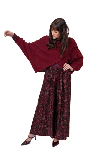 Woman wearing a burgundy oversized sweater and patterned skirt on a white background