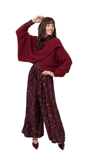 Woman wearing a burgundy sweater and patterned pants on a white background
