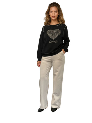 Woman wearing a black sweater with a heart design and beige pants on a white background