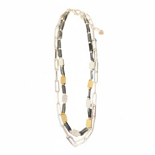 A multi-strand beaded necklace with black, silver, and gold rectangular beads, laid flat on a speckled brown granite countertop.