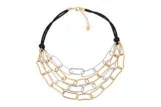 A multi-strand statement necklace featuring black braided cords and layered gold and silver chain link bibs, resting on a speckled gray stone surface.