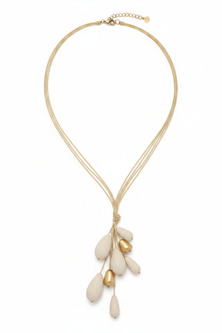 A multi-strand gold necklace with large cream-colored teardrop beads and small gold accent beads, laid out on a speckled dark countertop.