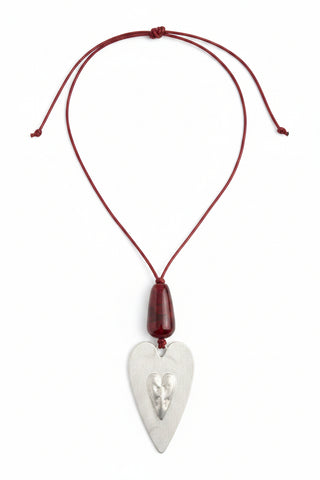 A red cord necklace with a translucent red teardrop-shaped bead and a white heart-shaped pendant engraved with a design, resting on a speckled granite countertop.