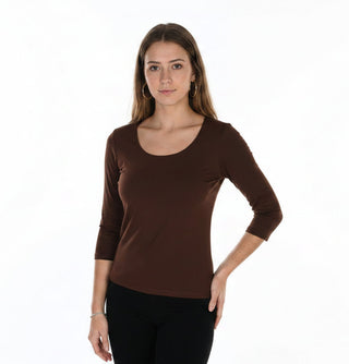 A woman modeling a white three-quarter sleeve scoop-neck top paired with black pants, photographed against a seamless white studio background.
