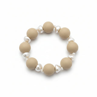 A beaded stretch bracelet featuring matte cream-colored round beads and small white irregular shell beads, displayed on a brown and black speckled granite surface.