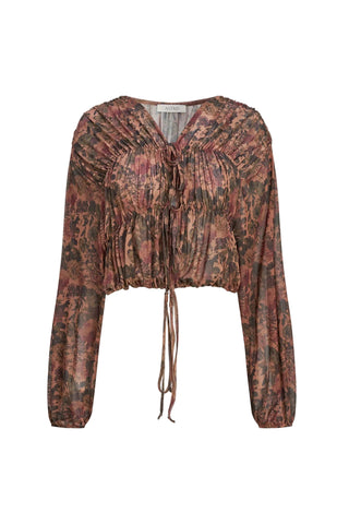 A long-sleeve cropped blouse with an abstract, painterly pattern in muted earthy tones of brown, terracotta, and burgundy, featuring a gathered smocked bodice, V-neckline, and front tie closures, shown against a light gray background.