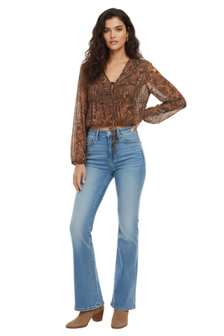 A model wearing a brown patterned long-sleeve blouse and light-wash blue flare jeans, standing against a plain white studio background.