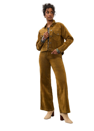 A model stands in a studio wearing a matching two-piece corduroy set in a warm mustard-brown color, consisting of a cropped button-up jacket and wide-leg pants, paired with beige heeled boots.
