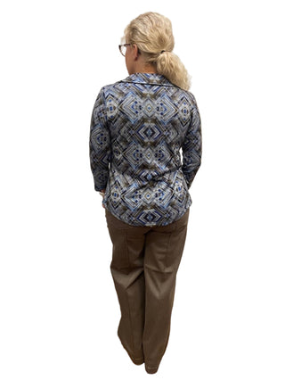 Person wearing a blue patterned shirt and brown pants standing in front of a white curtain.
