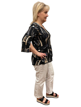 Woman trying on a black and white patterned top and white pants in a fitting room.