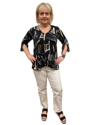 Woman wearing a black and white patterned top and white pants in a fitting room.